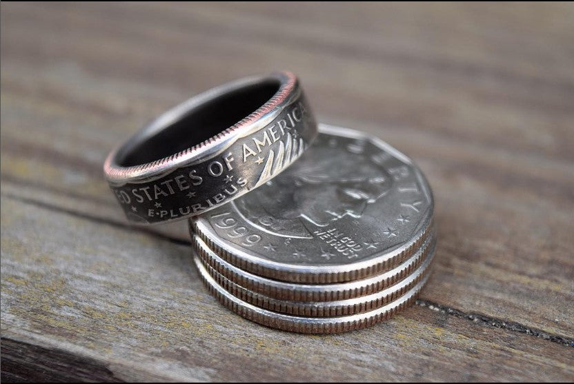 Stack of 4 Susan B Anthony Dollar Coins on a wood background with a handmade Susan B Anthony coin ring leaning on top of the stacked coins.