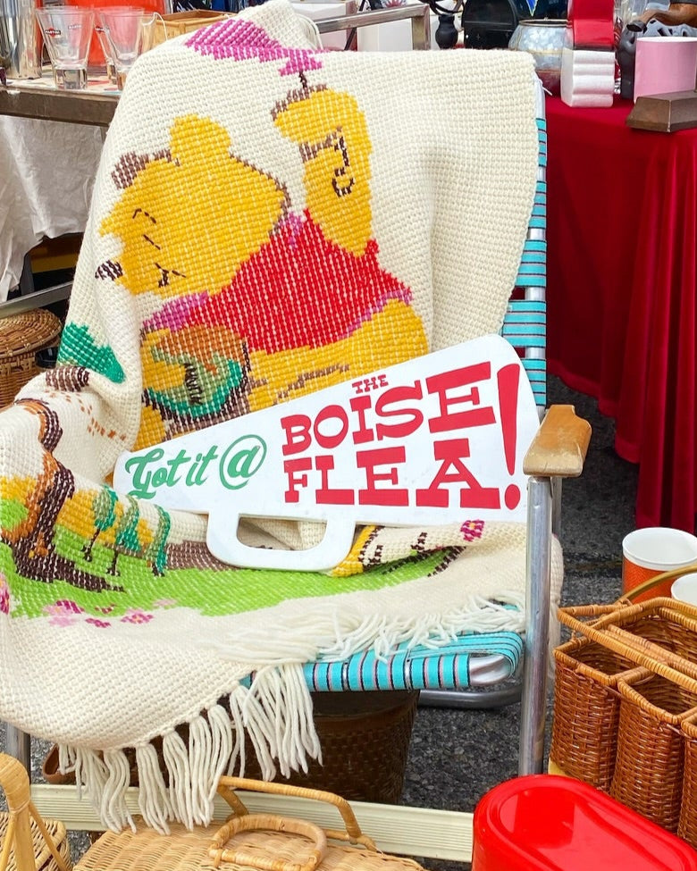 Winnie the Pooh Blanket on a old folding chair with a wooden microphone shaped sign saying "Get it @ the Boise Flea!". - Mountainstruck Coin Jewelry