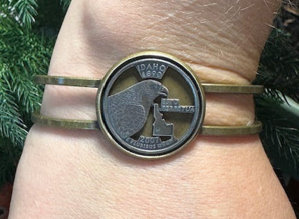Idaho State Quarter Cut Out Coin in a bronze bracelet on a wrist in front of a pine tree. - Mountainstruck Coin Jewelry