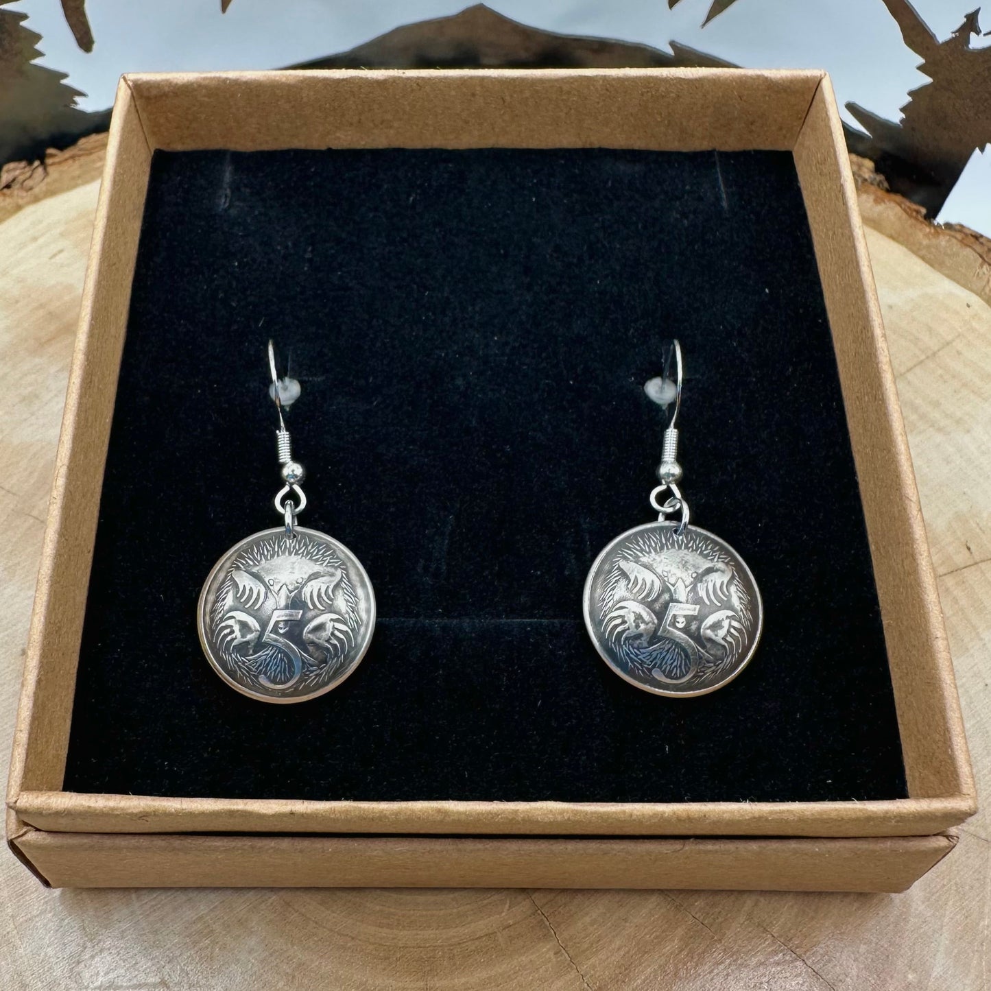 Australia Echidna 5 Cent Domed Coin Earrings in a brown kraft box on a black velvet background on top of a wood round with a metal mountain and tree display. - Mountainstruck Coin Jewelry