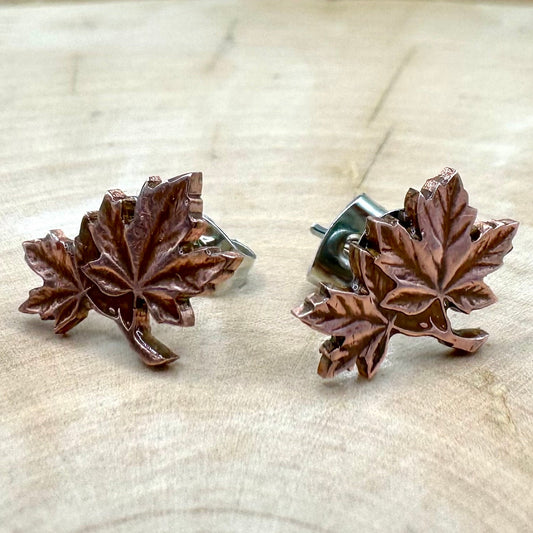 Canada Maple Leaf Penny Stud Coin Earrings on a light wood round metal mountain background.
- Mountainstruck Coin Jewelry