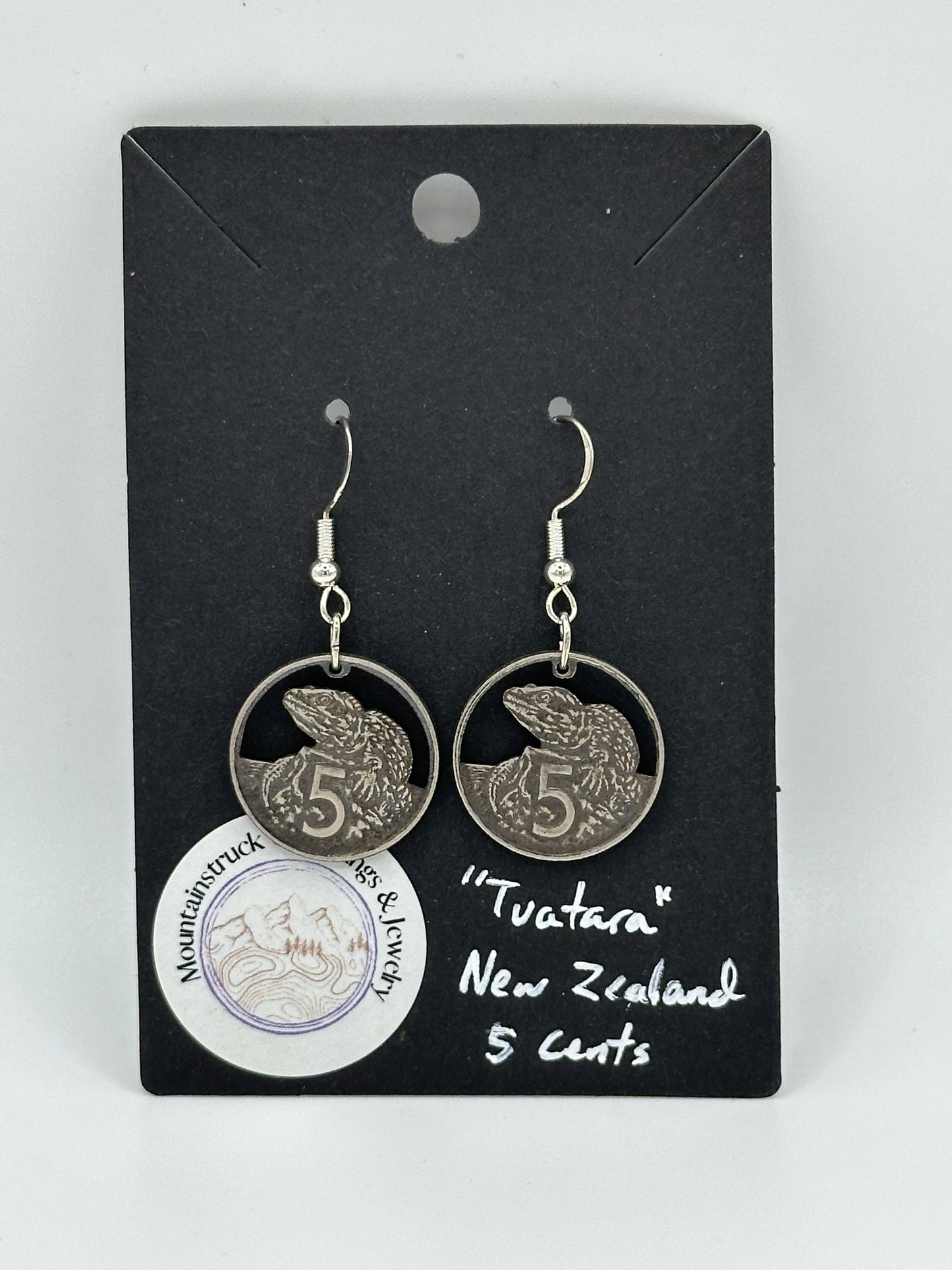 Tuatara New Zealand 5 Cents Hand Cut Coin Earrings on a black background with a round Mountainstruck Coin Jewelry sticker in bottom left corner.