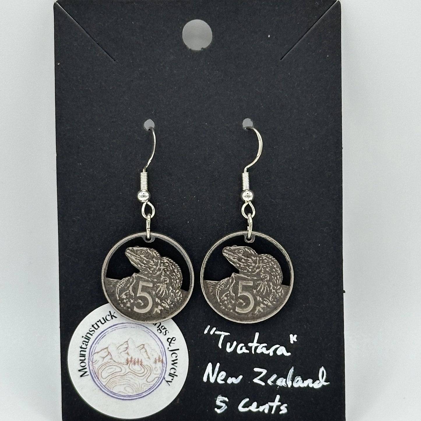 Tuatara New Zealand 5 Cents Hand Cut Coin Earrings on a black background with a round Mountainstruck Coin Jewelry sticker in bottom left corner.
