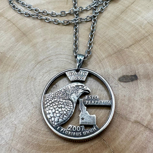 U.S. Idaho State Quarter Hand Cut Coin Necklace with a stainless steel chain on a wood background. - Mountainstruck Coin Jewelry