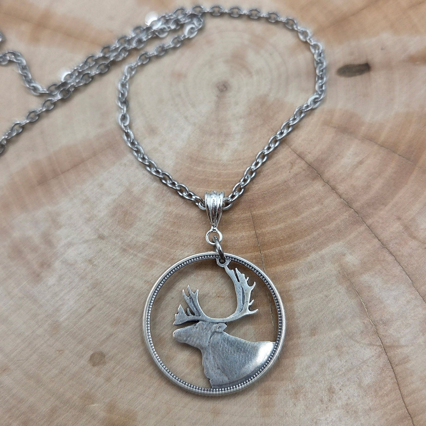 Canada Caribou 25 Cents hand cut coin necklace with a stainless steel chain on a wood background. - Mountainstruck Coin Jewelry