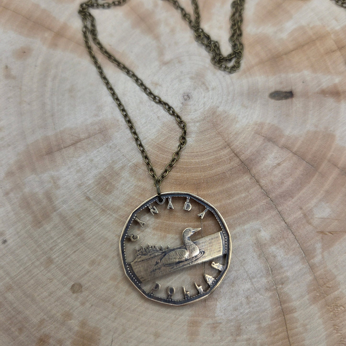 Canadian Loonie 1 Dollar Hand Cut Coin Necklace with bronze chain on a wood background. - Mountainstruck Coin Jewelry