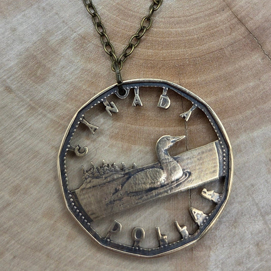 Canadian Loonie 1 Dollar Hand Cut Coin Necklace with bronze chain on a wood background. - Mountainstruck Coin Jewelry