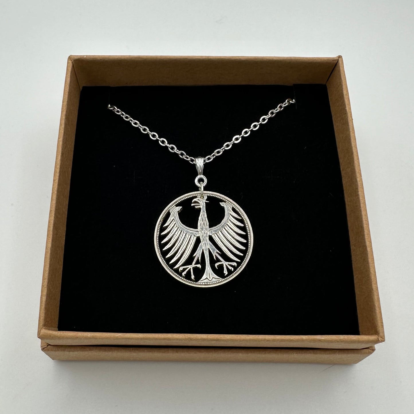 Germany Silver Eagle 5 Mark Hand Cut Coin Necklace in a brown kraft box on a black velvet background. - Mountainstruck Coin Jewelry