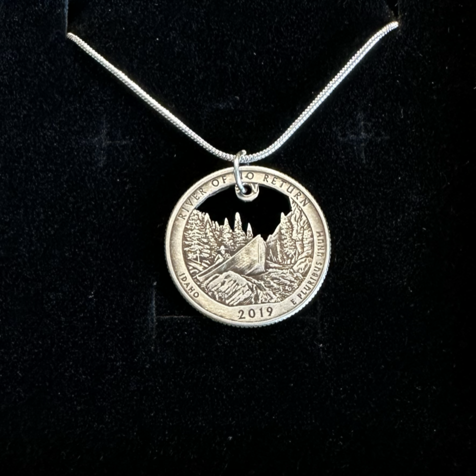 Idaho "River of No Return" Hand Cut Quarter Necklace with a snake chain in a brown kraft box on a black velvet background. - Mountainstruck Coin Jewelry