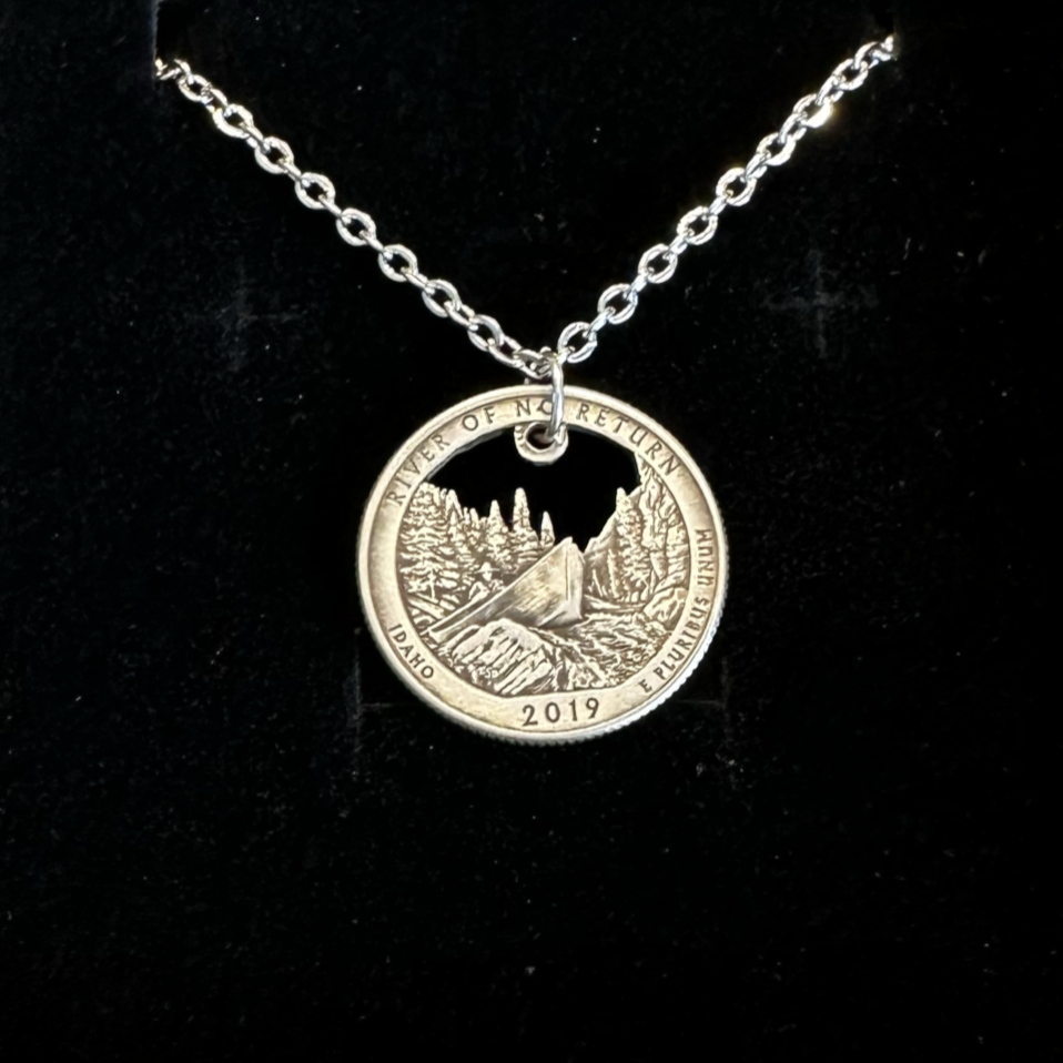 Idaho "River of No Return" Hand Cut Quarter Necklace with a stainless chain in a brown kraft box on a black velvet background. - Mountainstruck Coin Jewelry