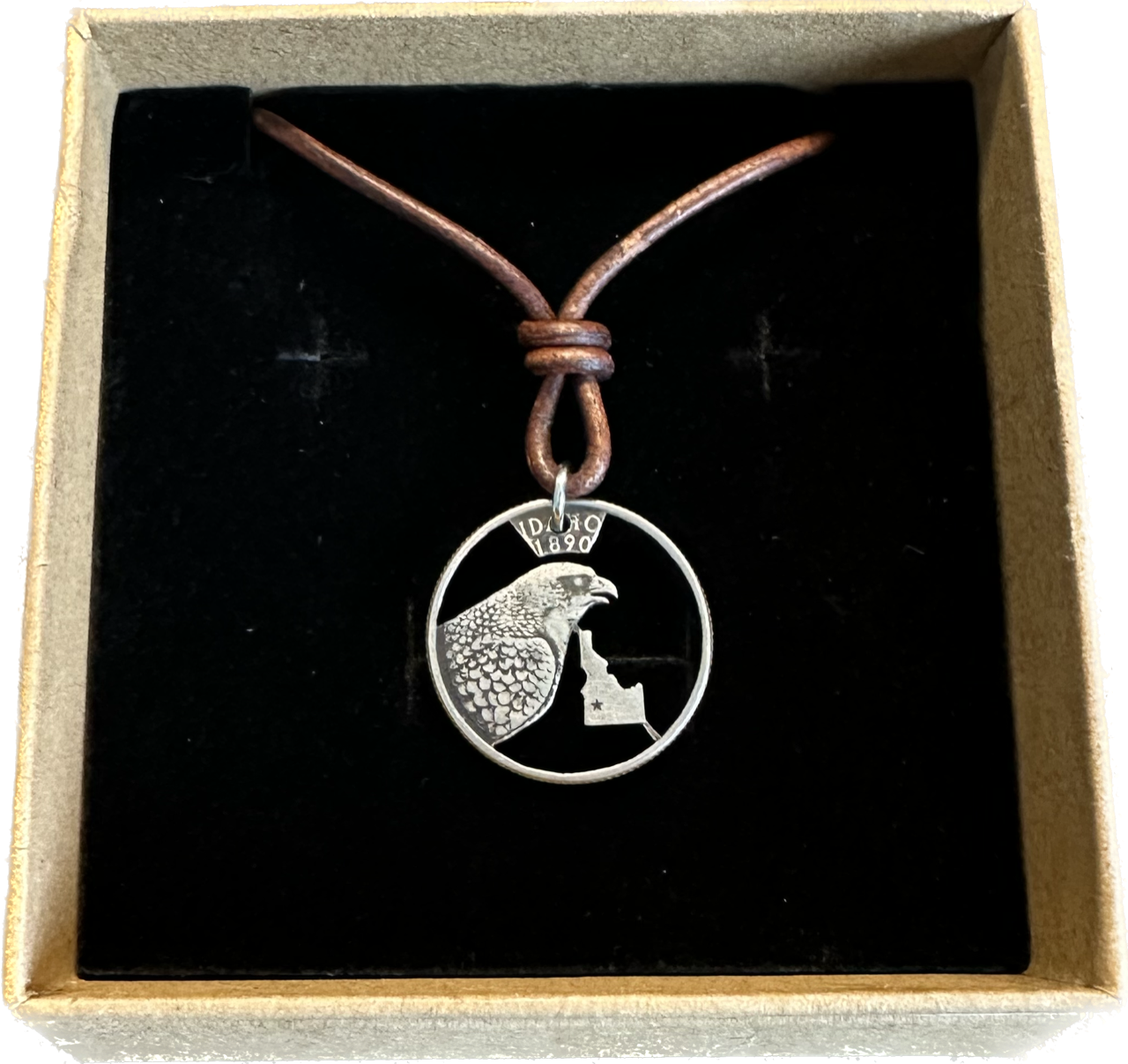 Idaho State Quarter Hand Cut Coin Necklace with a leather cord in a brown kraft box on a black velvet background. - Mountainstruck Coin Jewelry