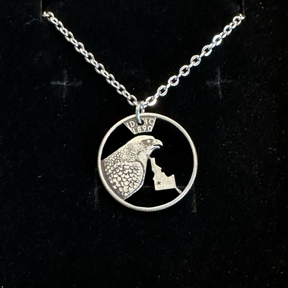 Idaho State Quarter Hand Cut Coin Necklace with a stainless chain in a brown kraft box on a black velvet background. - Mountainstruck Coin Jewelry
