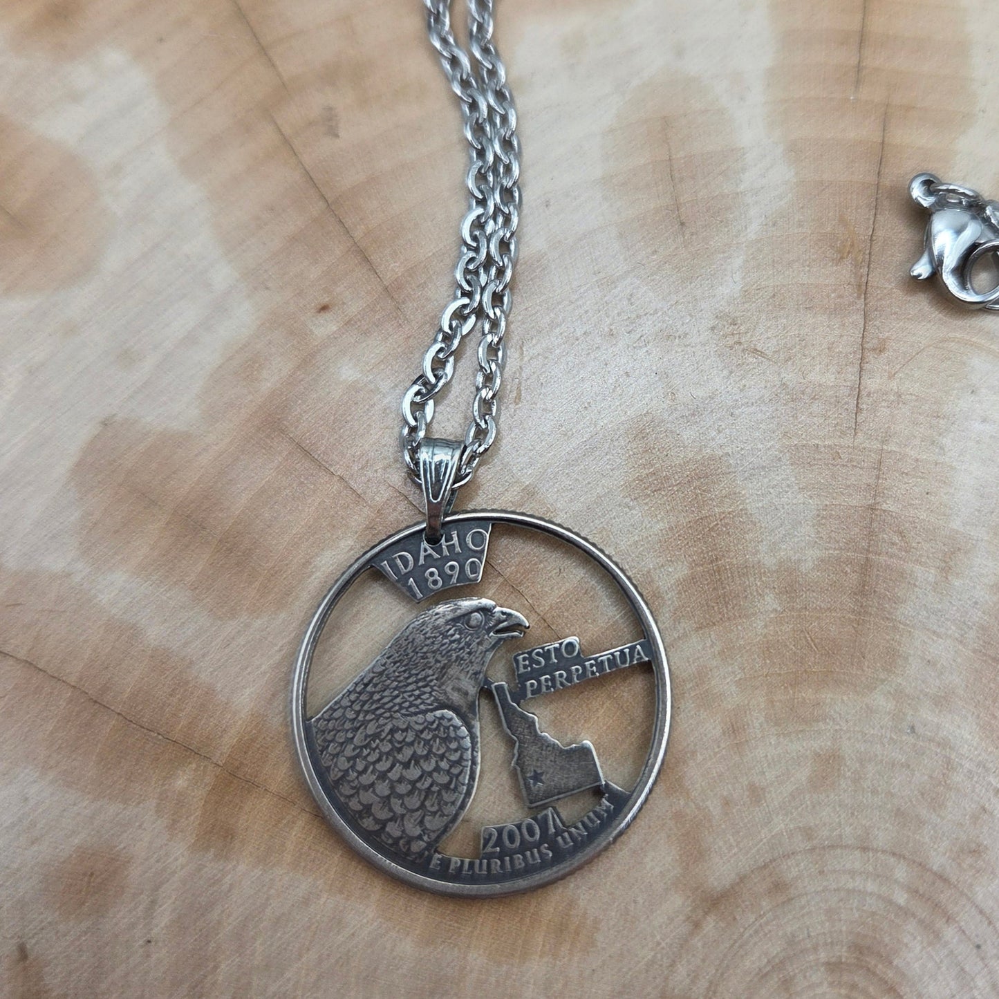 Idaho State Quarter Hand Cut Coin Necklace with a stainless steel chain on a wood background. - Mountainstruck Coin Jewelry