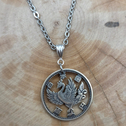 Japan Phoenix 100 Yen Silver Hand Cut Coin Necklace on a wood background. - Mountainstruck Coin Jewelry