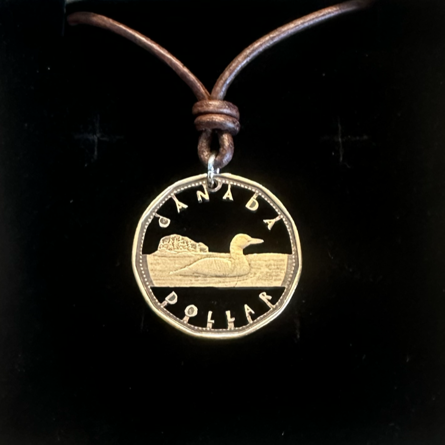 Canadian Loonie 1 Dollar Hand Cut Coin Necklace with a leather cord on a black velvet background. - Mountainstruck Coin Jewelry
