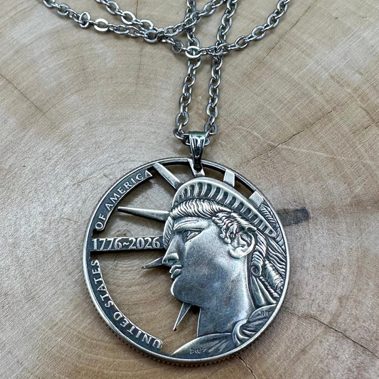 U.S. Half Dollar Hand Cut Coin Necklace (front) with a stainless chain on a light wood background. - Mountainstruck Coin Jewelry