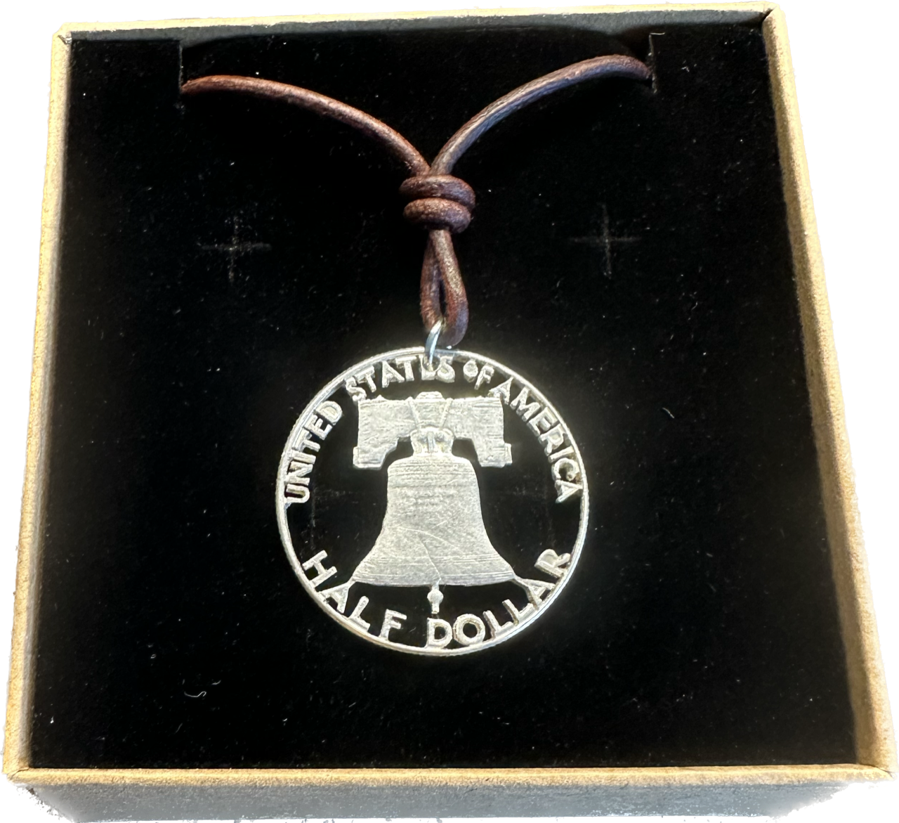 U.S. Cracked Liberty Bell Half Dollar Hand Cut Coin Necklace with a leather cord in a brown kraft box on a black velvet background. - Mountainstruck Coin Jewelry
