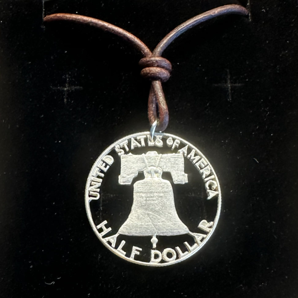 U.S. Cracked Liberty Bell Half Dollar Hand Cut Coin Necklace with a leather cord in a brown kraft box on a black velvet background. - Mountainstruck Coin Jewelry
