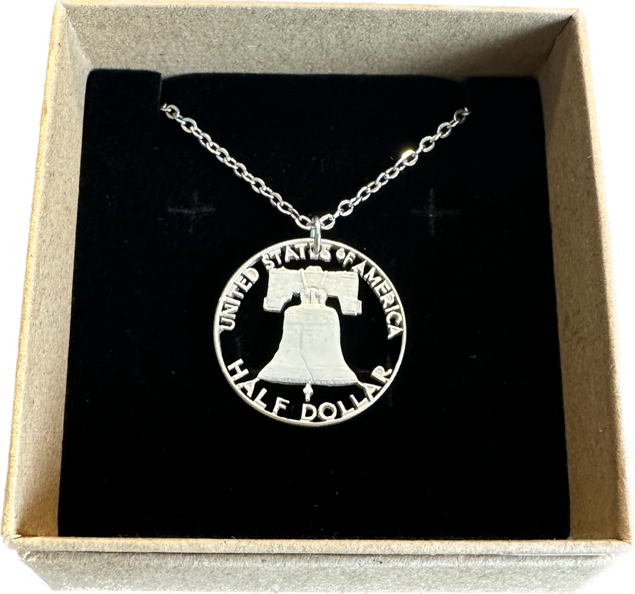 U.S. Cracked Liberty Bell Half Dollar Hand Cut Coin Necklace with a stainless chain in a brown kraft box on a black velvet background. - Mountainstruck Coin Jewelry
