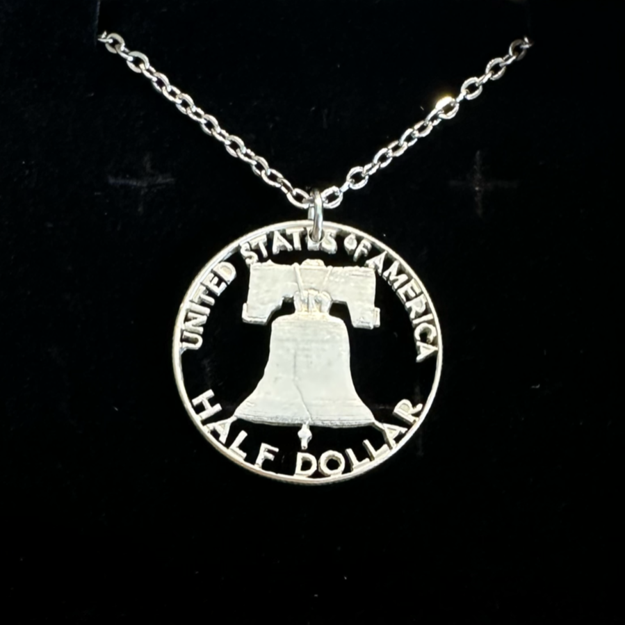 U.S. Cracked Liberty Bell Half Dollar Hand Cut Coin Necklace with a stainless chain in a brown kraft box on a black velvet background. - Mountainstruck Coin Jewelry