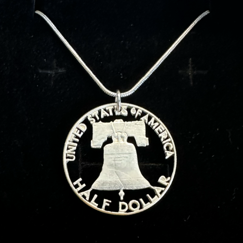 U.S. Cracked Liberty Bell Half Dollar Hand Cut Coin Necklace with a snake chain in a brown kraft box on a black velvet background. - Mountainstruck Coin Jewelry