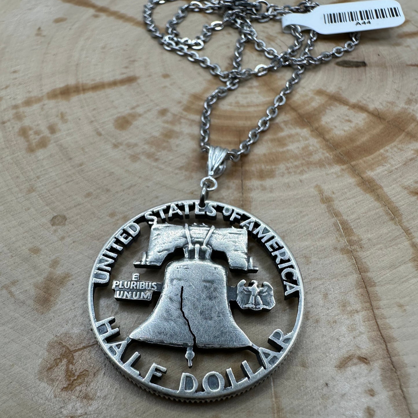 Cracked Liberty Bell U.S. Half Dollar Hand Cut Coin Necklace with stainless chain on a wood background. - Mountainstruck Coin Jewelry