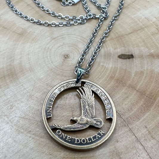 U.S. Flying Eagle Sacagawea One Dollar Hand Cut Coin Necklace with snake chain on a light wood round. - Mountainstruck Coin Jewelry