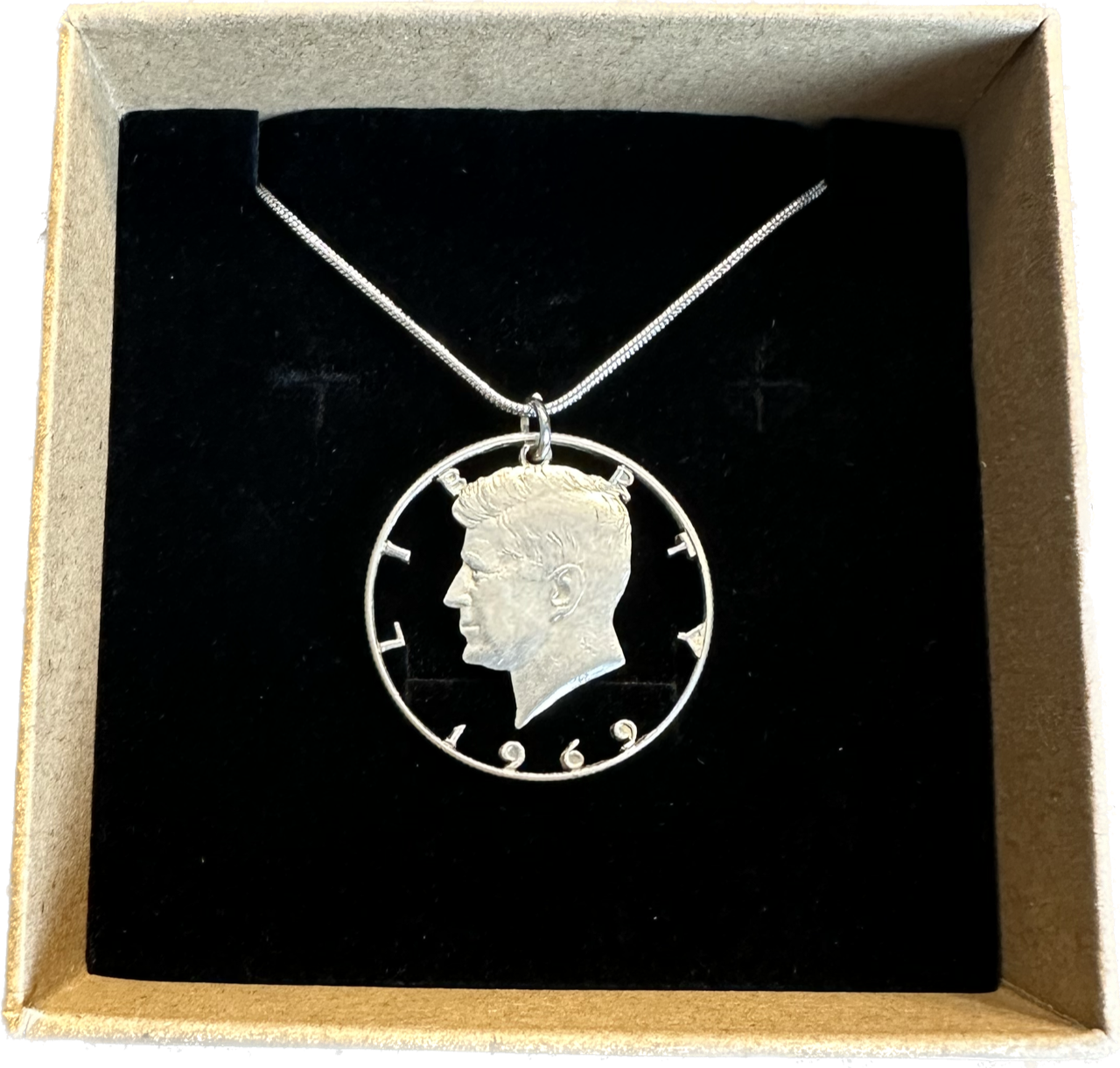 U.S. JFK Half Dollar Hand Cut Silver Coin Necklace with snake chain in a brown kraft box on black velvet background. - Mountainstruck Coin Jewelry