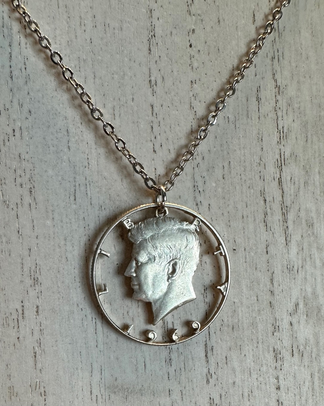 U.S. JFK Half Dollar Hand Cut Silver Coin Necklace with stainless chain on a light wood background. - Mountainstruck Coin Jewelry