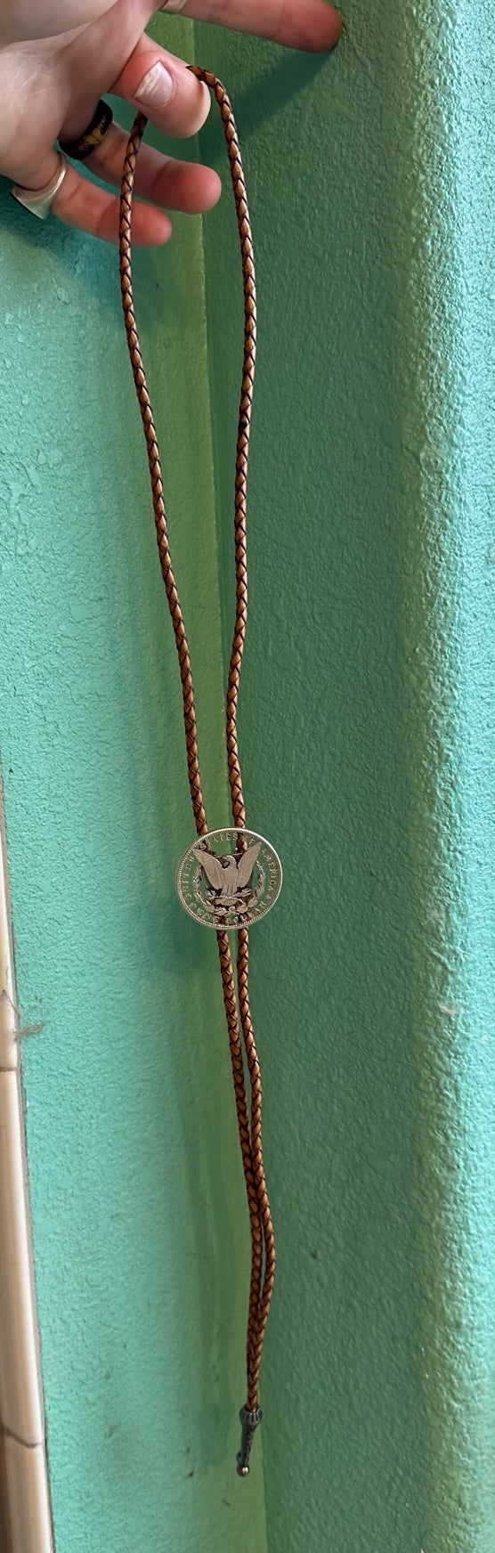 U.S. Morgan Hand Cut Silver Dollar Coin Bolo Tie (reverse) hanging in front of teal background. - Mountainstruck Coin Jewelry