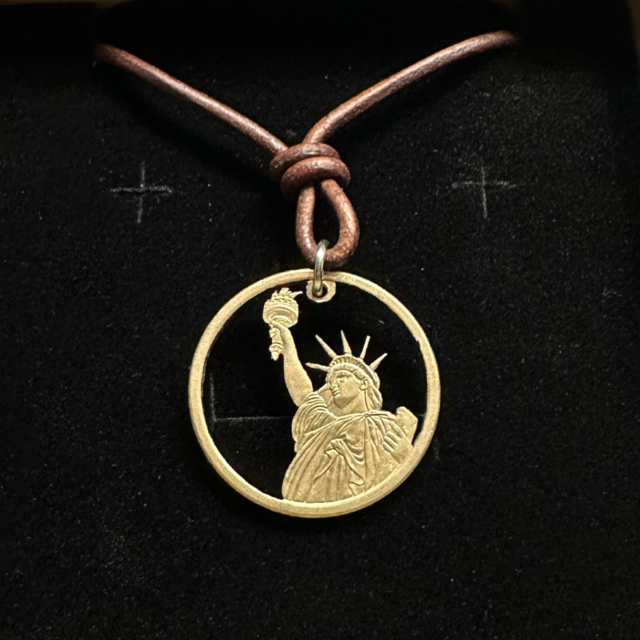 U.S. Statue of Liberty Gold Dollar Hand Cut Coin Necklace with leather cord in a brown kraft box on a black velvet background. - Mountainstruck Coin Jewelry
