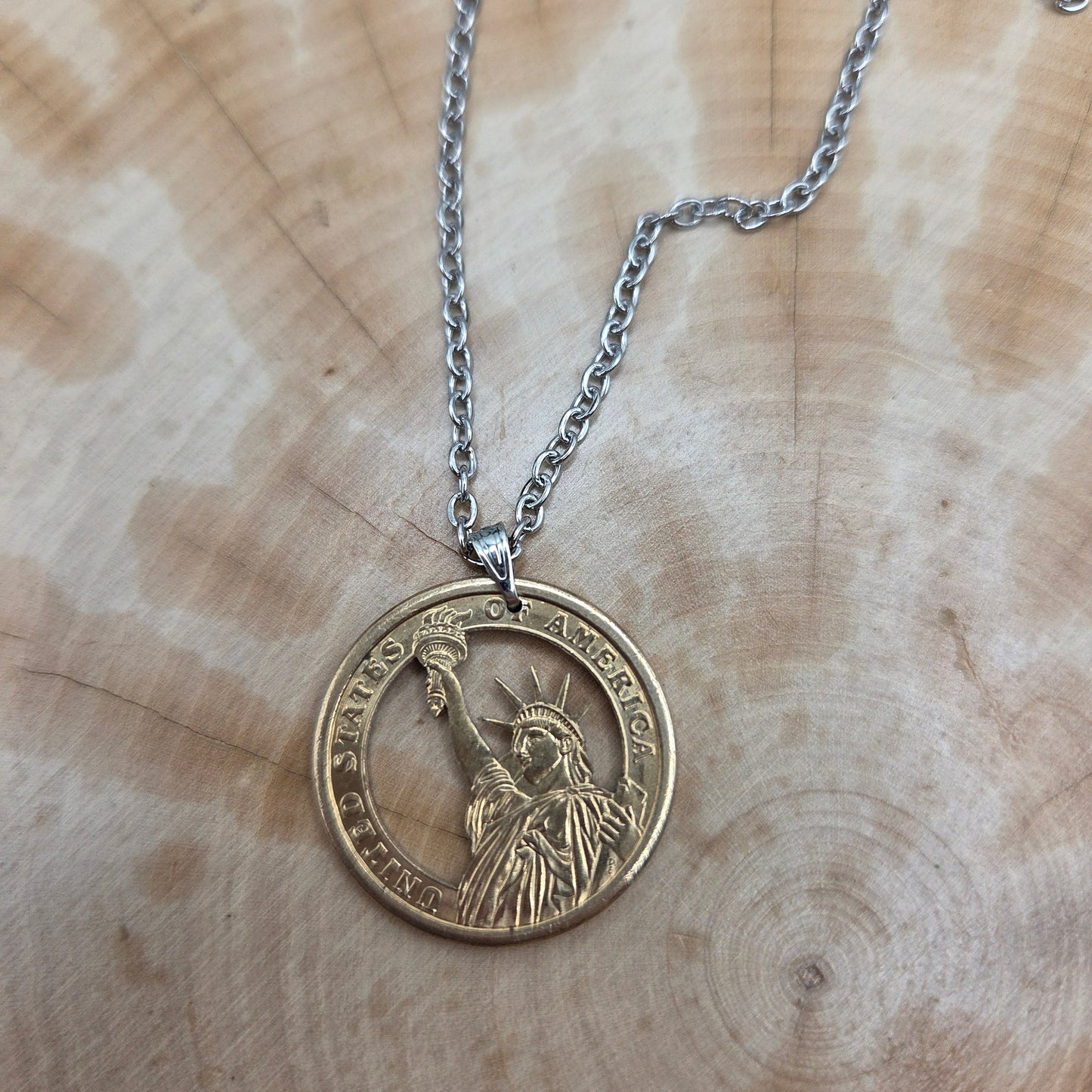 U.S. Statue of Liberty Gold Dollar Hand Cut Coin Necklace with a stainless chain on a wood background. - Mountainstruck Coin Jewelry