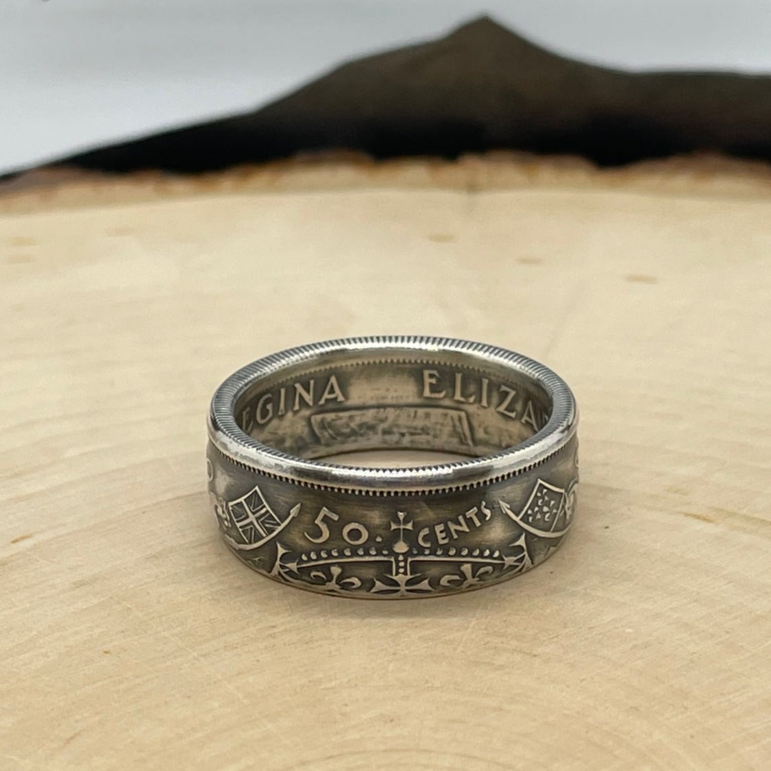 Canada 50 Cents Silver Coin Ring (Lion + Unicorn) on a light wood round with mountain outline in the background. - Mountainstruck Coin Jewelry