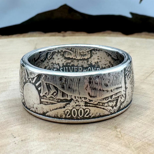 U.S. 1oz 999 Silver Eagle $1 Coin Ring on a light wood round with a metal mountain background. - Mountainstruck Coin Jewelry