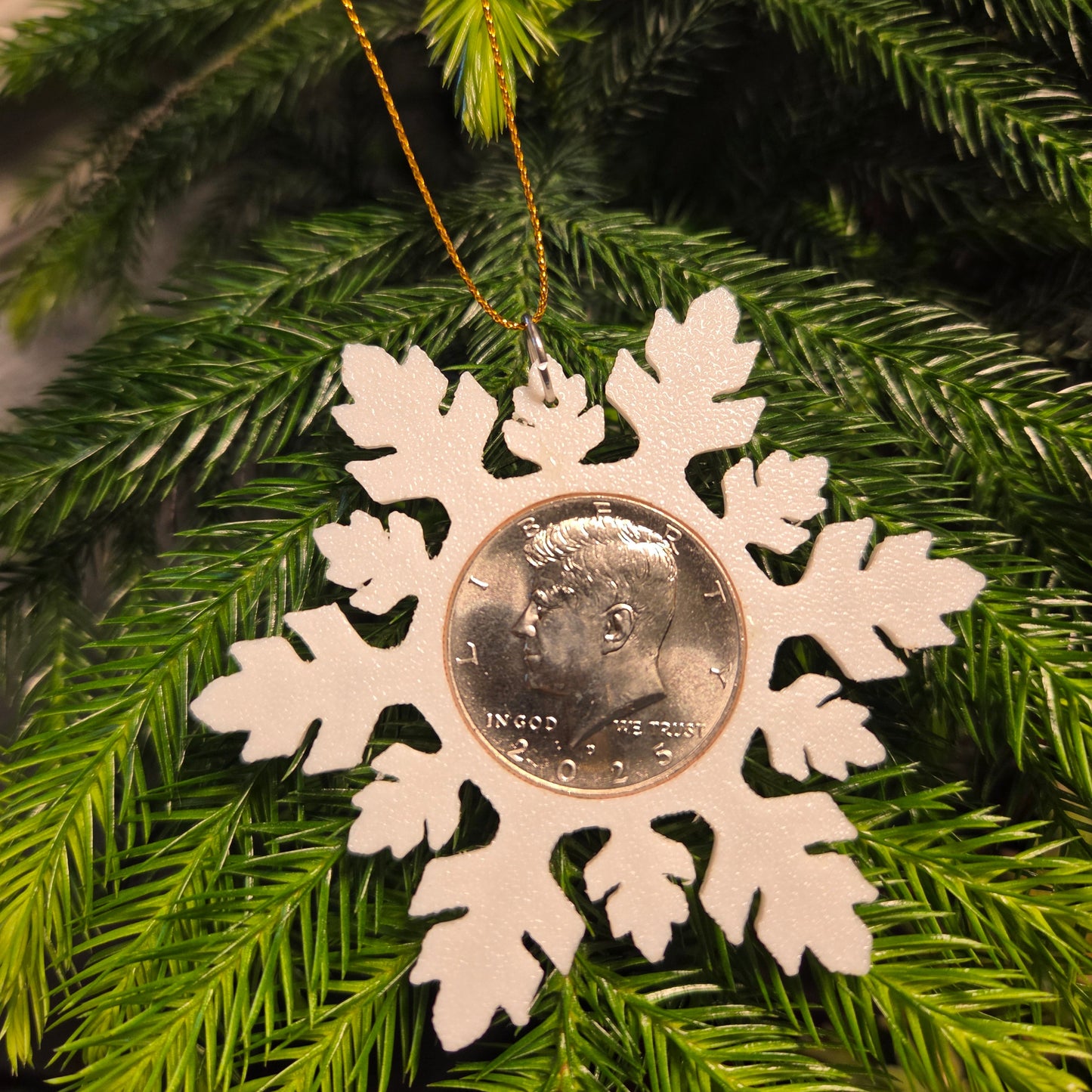 2025 Half Dollar Christmas Ornament with an uncirculated half dollar cased inside a white 3D printed snowflake with golden tassel on a green pine tree. - Mountainstruck Coin Jewelry