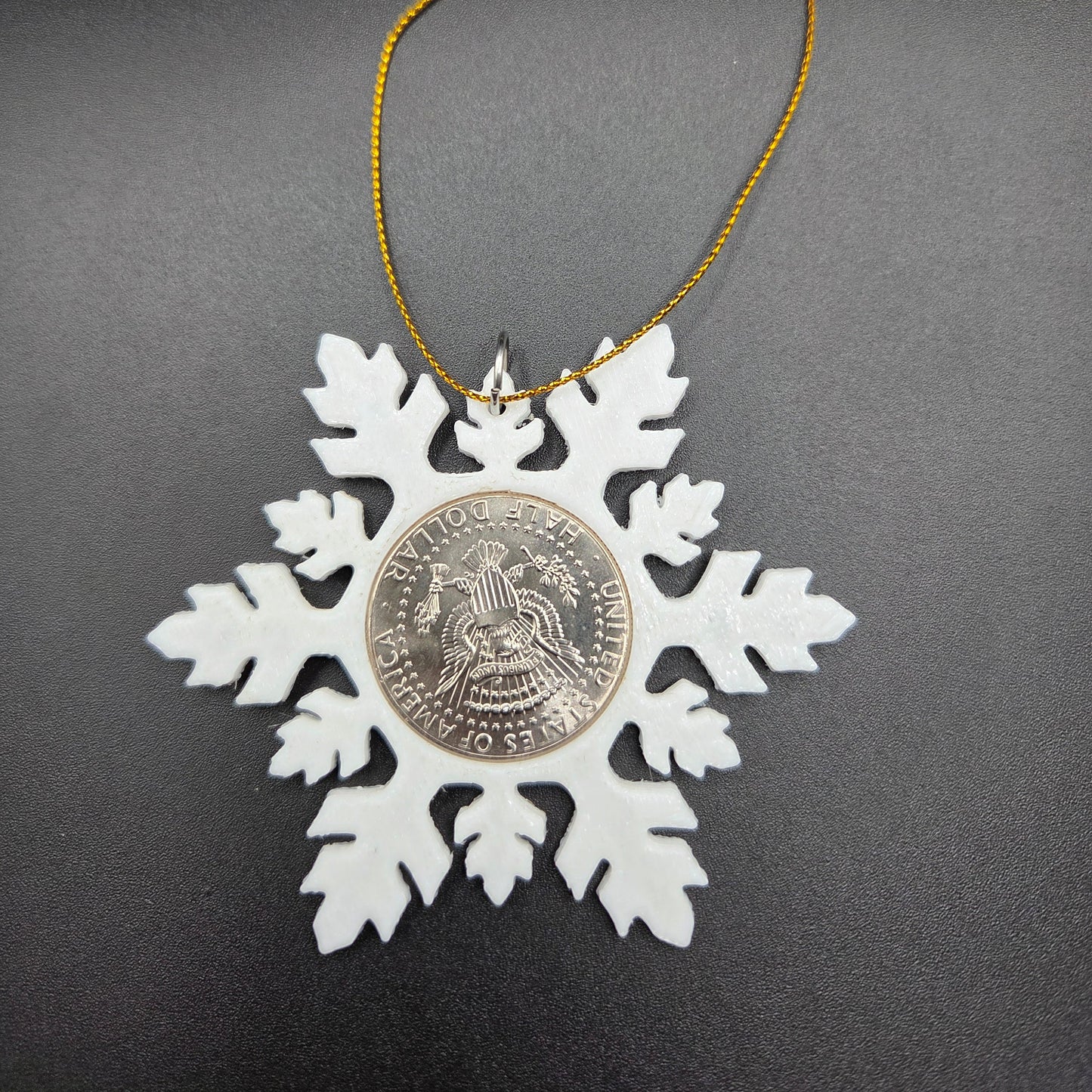 2025 Half Dollar Christmas Ornament with an uncirculated half dollar cased inside a white 3D printed snowflake with golden tassel on a black background. - Mountainstruck Coin Jewelry