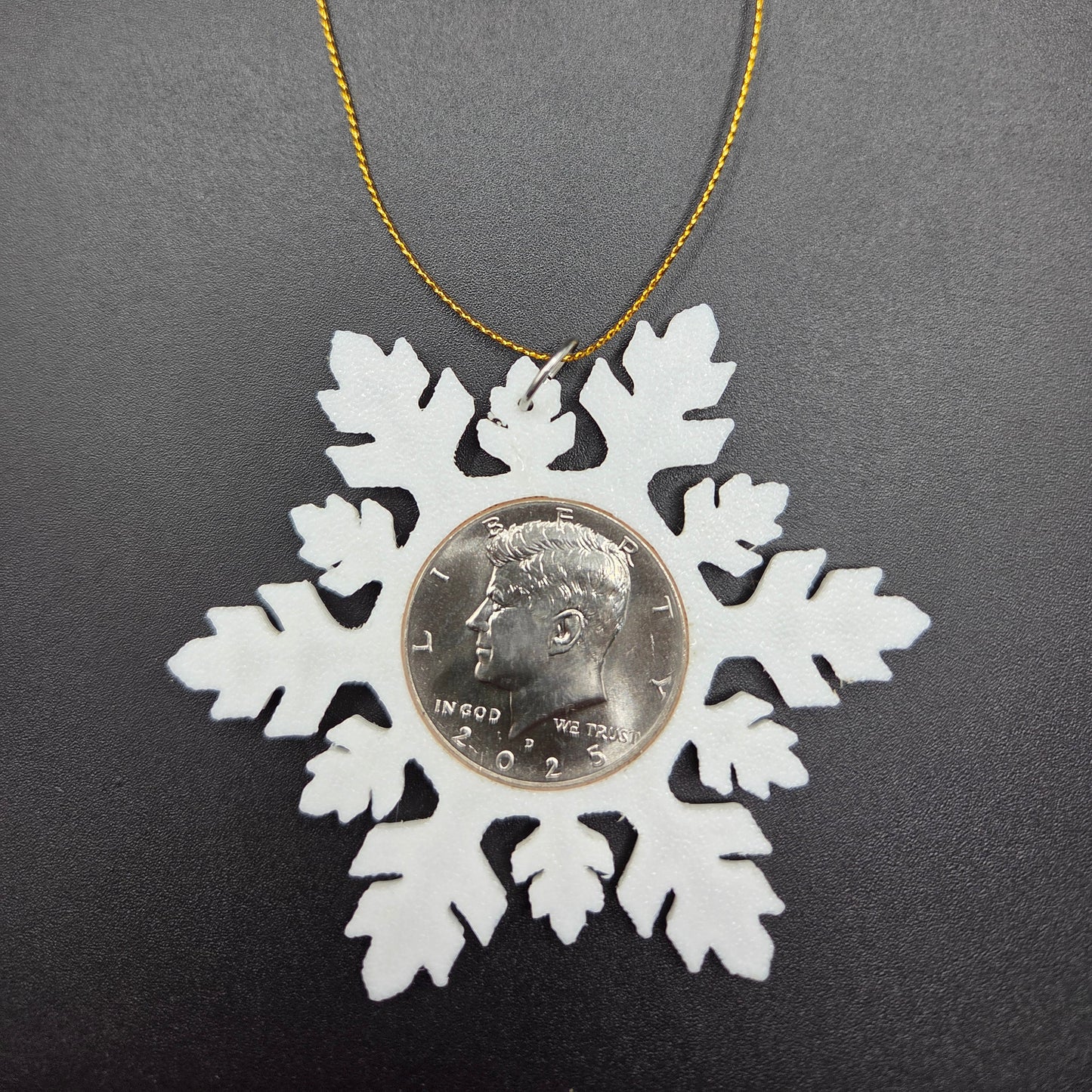 2025 Half Dollar Christmas Ornament with an uncirculated half dollar cased inside a white 3D printed snowflake with golden tassel on a black background. - Mountainstruck Coin Jewelry