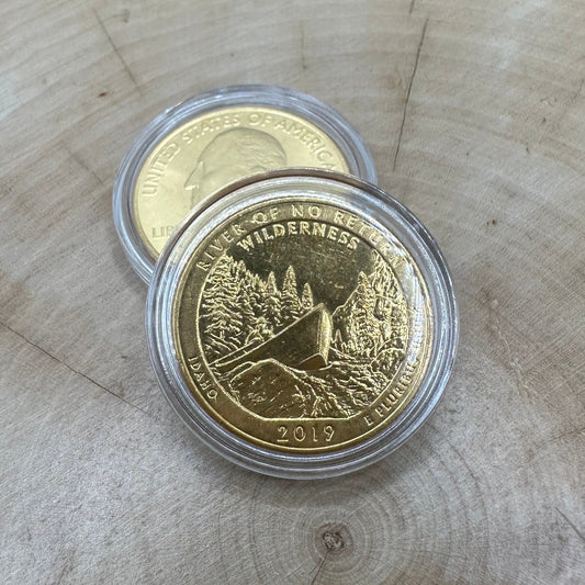 U.S. River of No Return Wilderness Quarter 24k Gold Plated Coin in a plastic case on a light wood round on top of the back of a U.S. River of No Return Wilderness Quarter 24k Gold Plated Coin in a plastic case.
- Mountainstruck Coin Jewelry