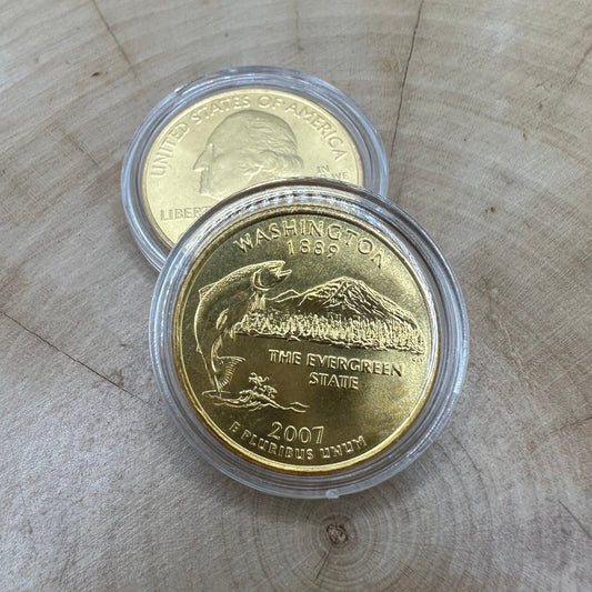 U.S. Washington Quarter 24k Gold Plated Coin in a plastic case on a light wood round on top of the back of a U.S. Washington Quarter 24k Gold Plated Coin in a plastic case.
- Mountainstruck Coin Jewelry