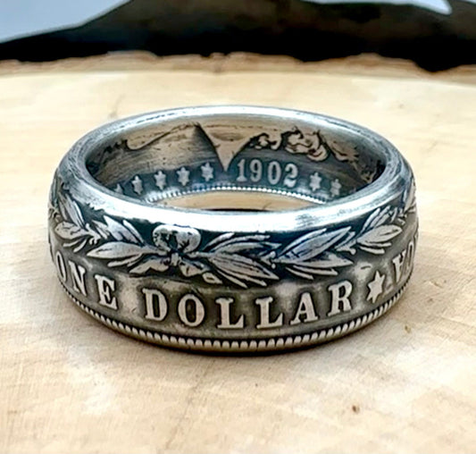 U.S. Morgan Dollar Silver Coin Ring patina on a light wood round with a metal mountain background. - Mountainstruck Coin Jewelry