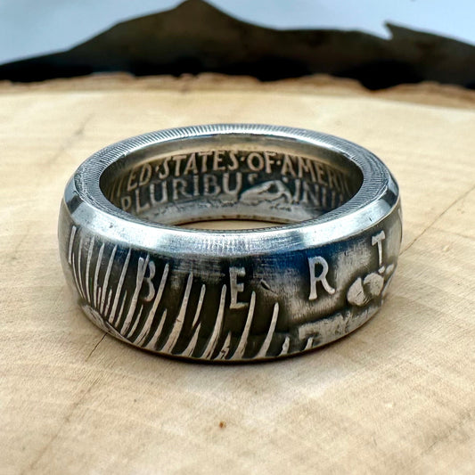 U.S. Peace Dollar Silver Coin Ring on a light wood round with a metal mountain background. - Mountainstruck Coin Jewelry