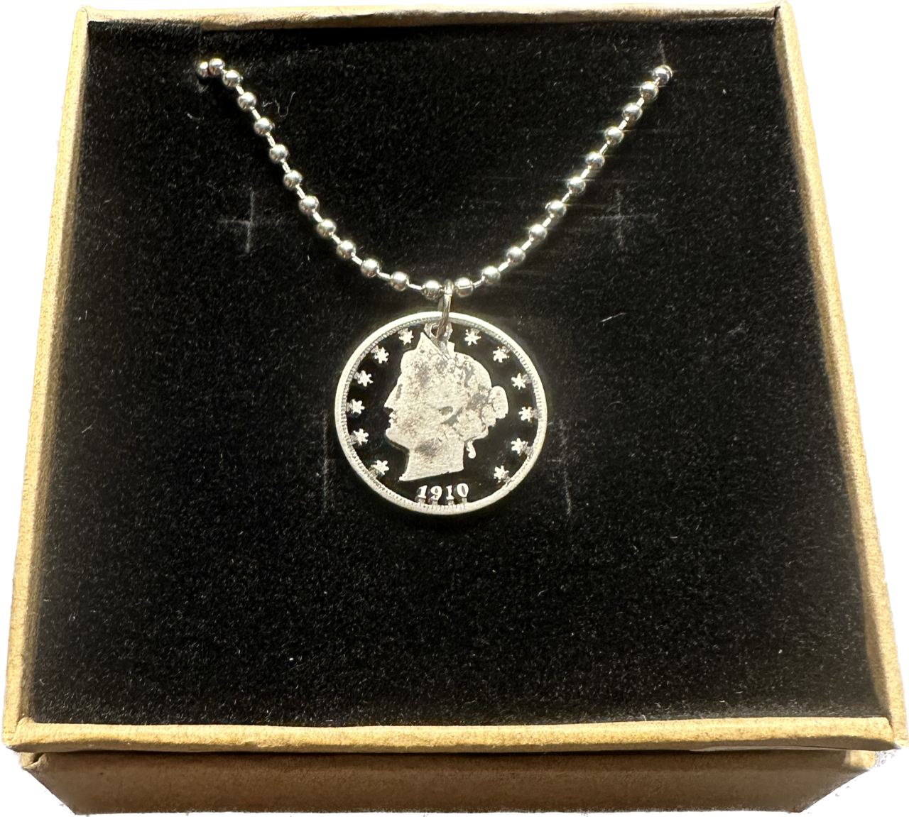 U.S. "V" Nickel Hand Cut Coin Necklace with a steel ball chain in a brown kraft box with a black velvet background.