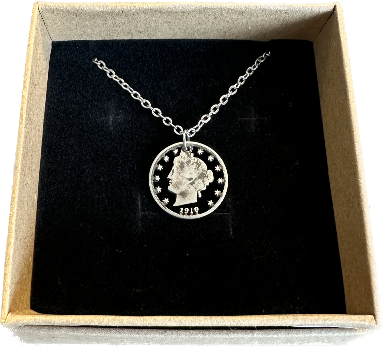 U.S. "V" Nickel Hand Cut Coin Necklace with a stainless chain in a brown kraft box with a black velvet background.