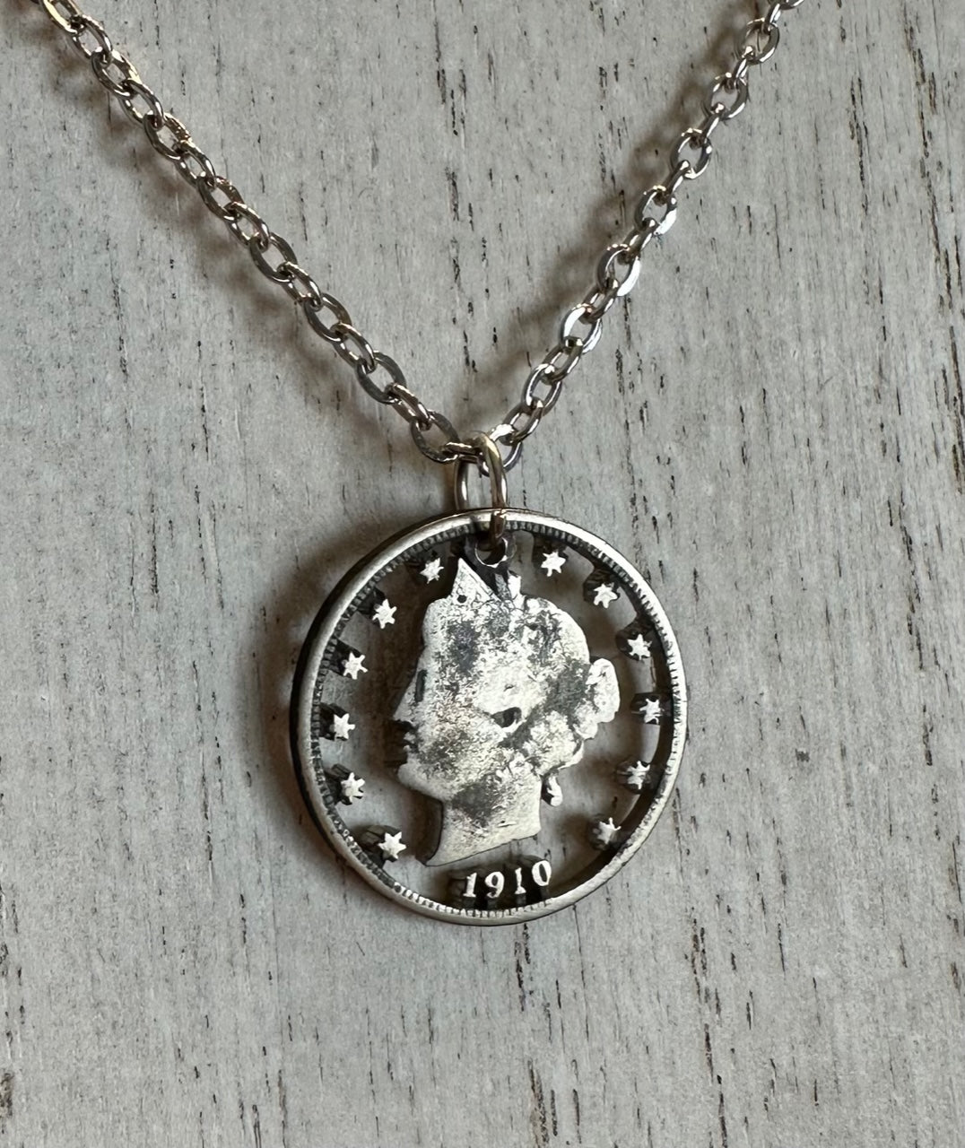 U.S. "V" Nickel Hand Cut Coin Necklace with a stainless chain on a white wood background.