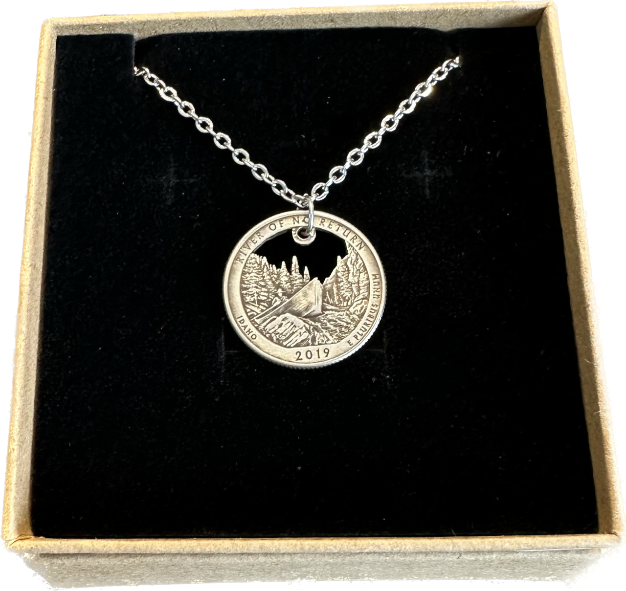 Idaho "River of No Return" Hand Cut Quarter Necklace with a stainless chain in a brown kraft box on a black velvet background.