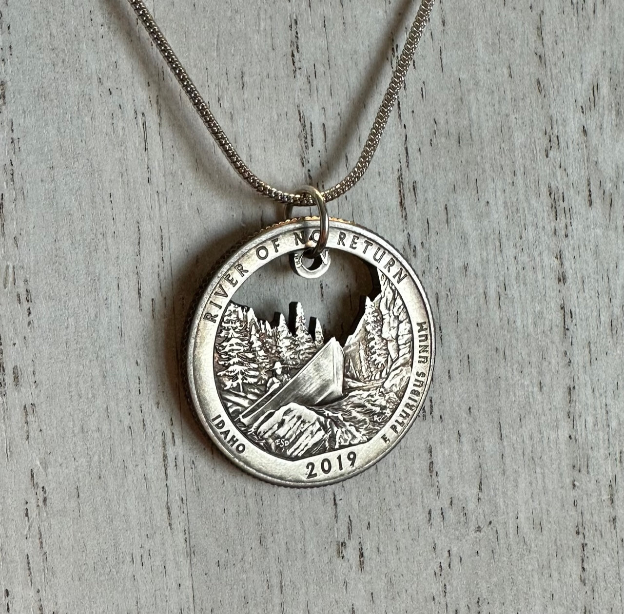 Idaho "River of No Return" Hand Cut Quarter Necklace with a snake chain on a white wood background.