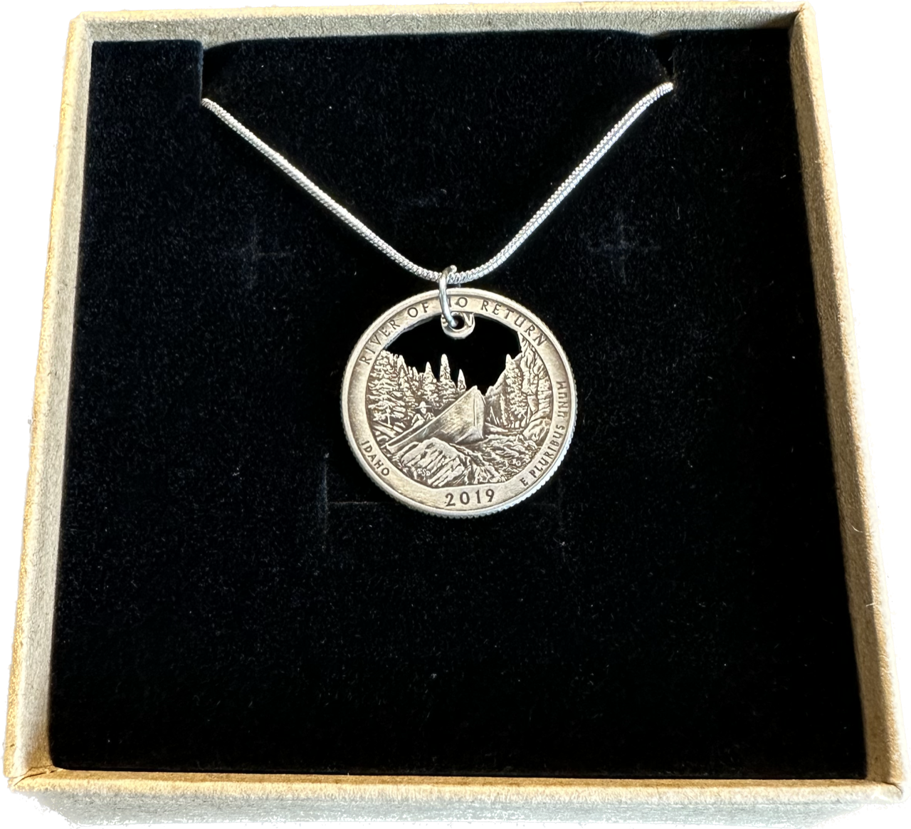 Idaho "River of No Return" Hand Cut Quarter Necklace with a snake chain in a brown kraft box on a black velvet background.