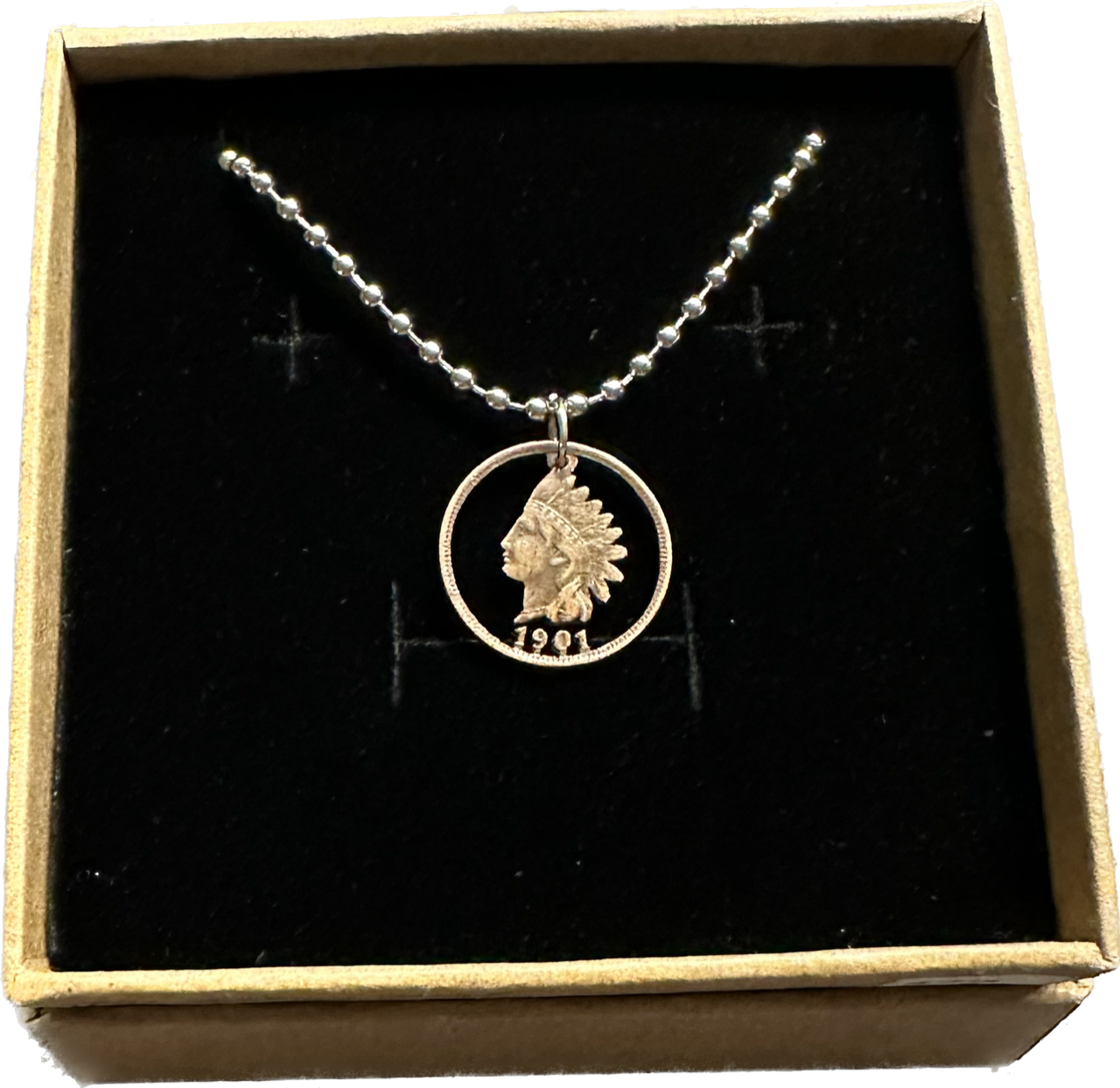 U.S. Indian Head Penny Coin Necklace with a steel ball chain in a brown kraft box on a black velvet background.