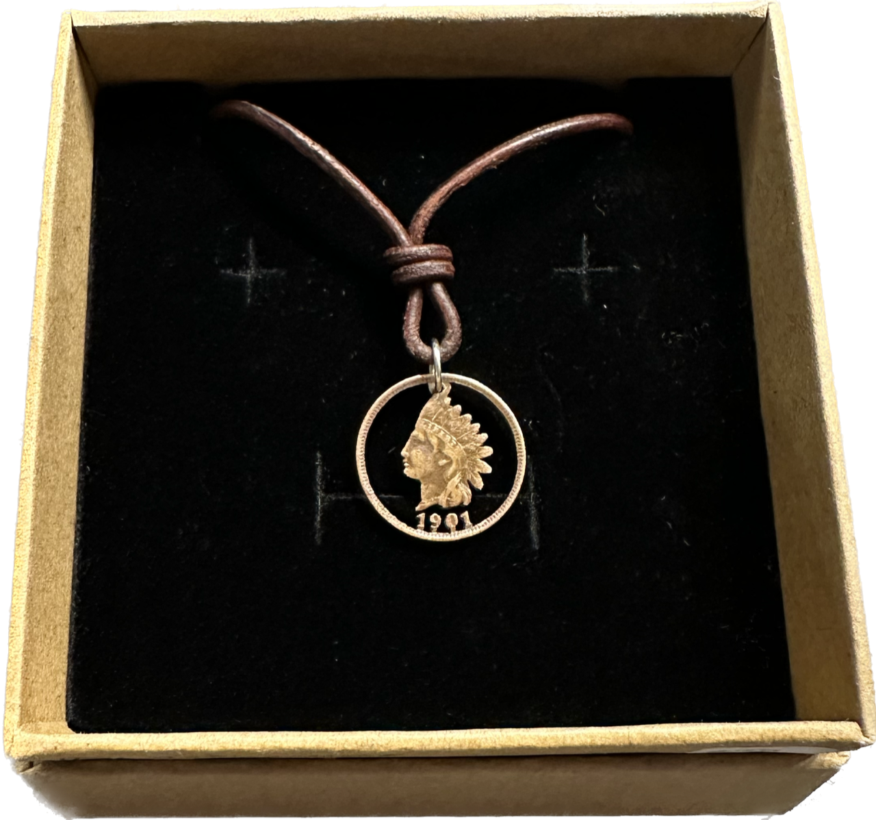 U.S. Indian Head Penny Coin Necklace with a leather cord in a brown kraft box on a black velvet background.