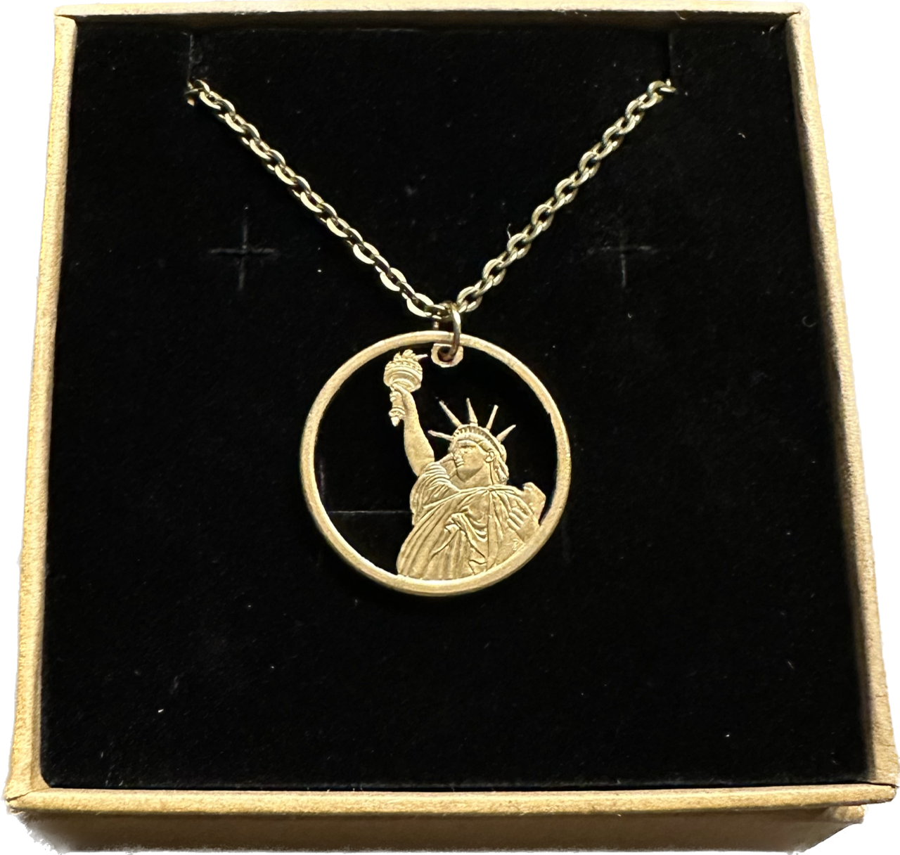 U.S. Statue of Liberty Gold Dollar Hand Cut Coin Necklace with a stainless chain in a brown kraft box on a black velvet background.